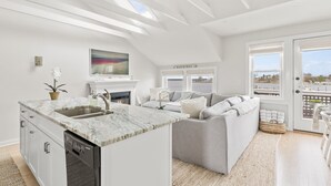 A modern kitchen with a marble countertop and a built-in dishwasher, a grey sofa, and a fireplace. - The Saltbox - Watch Hill's Award-Winning Waterfront Retreat.  (Westerly)