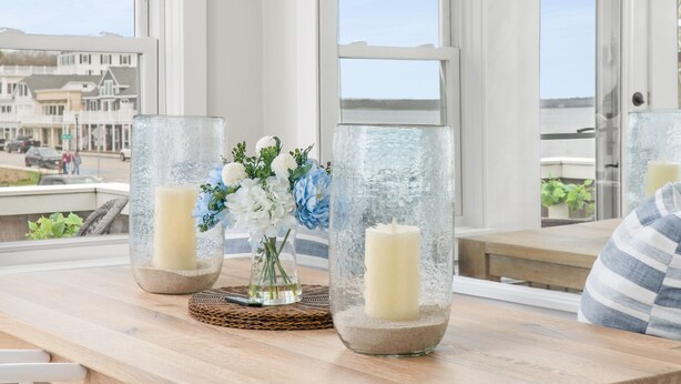 A wooden dining table with glass candle holders and a vase of flowers. - The Saltbox - Watch Hill's Award-Winning Waterfront Retreat.  (Westerly)