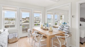 A bright room with a wooden dining table, white chairs, and a view of the harbor. - The Saltbox - Watch Hill's Award-Winning Waterfront Retreat.  (Westerly)