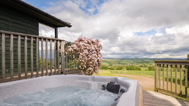 Ein Whirlpool auf einer Holzterrasse mit Blick auf eine grüne Landschaft.