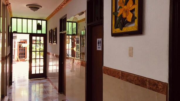 A hallway with a tiled floor, a door with a sign indicating a men's restroom, and a framed picture on the wall. - HOTEL DON JUAN  (Guadalajara de Buga)