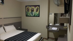 A hotel room with a bed, a bedside table, a mirror, a wall-mounted fan, and a painting of sunflowers. - HOTEL DON JUAN  (Guadalajara de Buga)