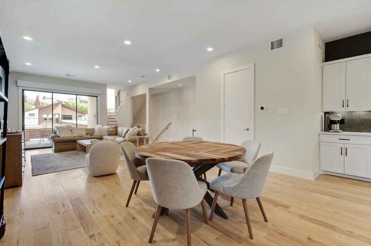 A modern living room with a wooden dining table, light-colored chairs, and a sofa.