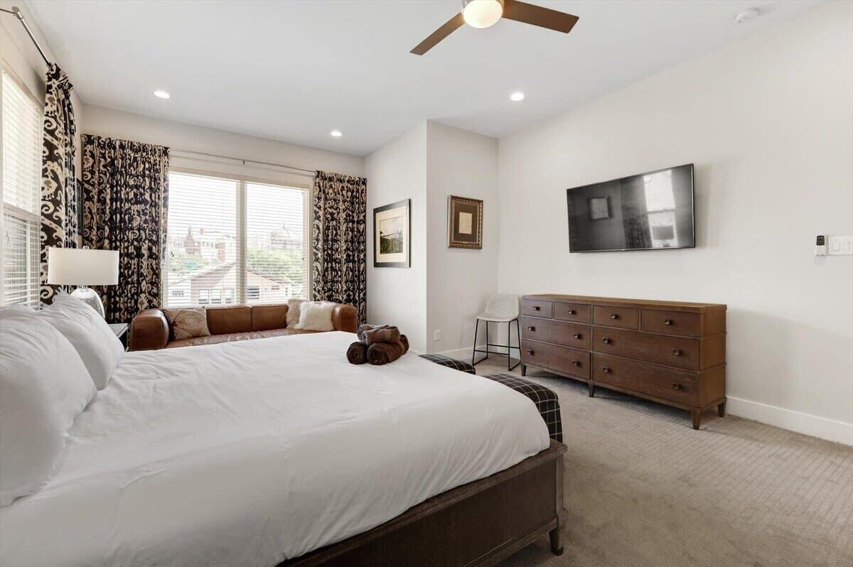 A bedroom with a large bed, a dresser, a TV, and a ceiling fan.