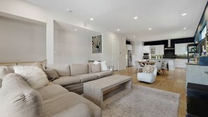 A modern living room with a sectional sofa, a coffee table, and a dining area with chairs. - Modern Luxury Townhouse | Uptown & Attractions (Dallas)