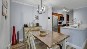 A modern kitchen with a central island, wooden dining table, and a hanging light fixture. - Heart of Dallas - Cozy Apt, 2Bed, Pool (30+ days) (Dallas)