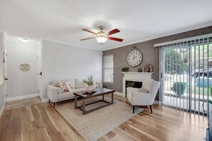 Ein Wohnzimmer mit weißem Sofa, Couchtisch, weißem Sessel, Kamin und einem großen Fenster mit Blick auf einen Swimmingpool.