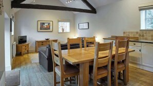 A dining area with a wooden table and chairs, a television, and a kitchen in the background. - Host & Stay | Derwent (Consett)