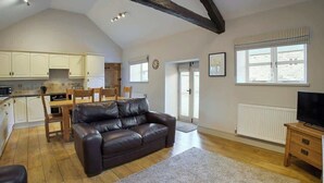 A spacious living room with a leather sofa, wooden dining table, and a TV stand. - Host & Stay | Derwent (Consett)