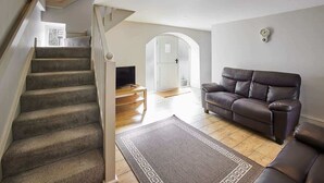 A staircase leading to a living room with a leather sofa, a TV, and a patterned rug. - Host & Stay | Mill (Consett)