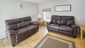 A living room with two dark leather sofas, a wooden coffee table, a lamp, a framed picture on the wall, and a window with a curtain. - Host & Stay | Mill (Consett)