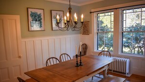 Comedor con mesa de madera, sillas, candelabro y ventana con vista a árboles.