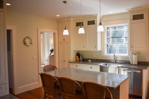 A kitchen with white cabinets, a central island with chairs, pendant lights, and a window. - Stately 4 bedroom home, less than a mile to Corporation Beach (Dennis)