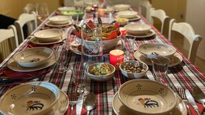 Una mesa de comedor dispuesta con platos, vasos y cubiertos, decorada con un mantel a cuadros y un arreglo floral central.