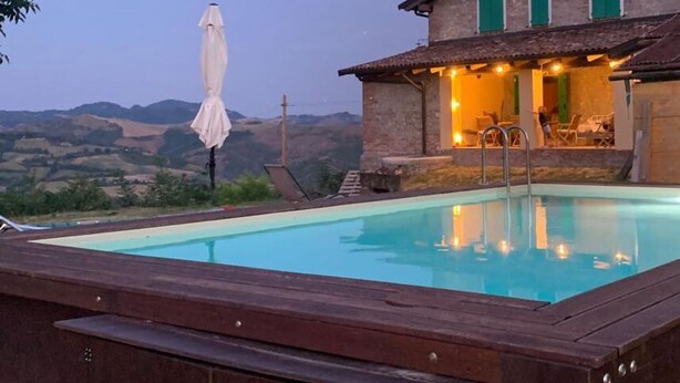 Un área de piscina con muelle de madera, una silla de descanso y una sombrilla.