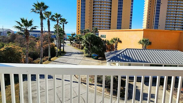 Un balcon donnant sur un quartier résidentiel, avec des palmiers et un immeuble doté de nombreux balcons.