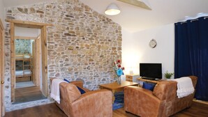 A cozy living room with a stone wall, wooden furniture, and a television. - Pen Dragon - 2 Bed Cottage - Penclawdd (Swansea)