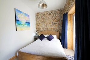 A bedroom with a wooden bed, stone wall, and a painting.