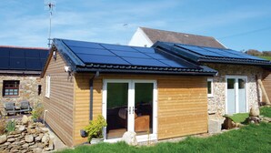 A wooden cabin with a stone exterior, a glass door entrance, and solar panels on the roof. - Pen Dragon - 2 Bed Cottage - Penclawdd (Swansea)