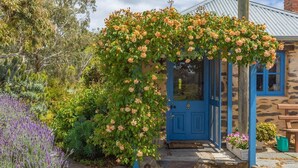 Um edifício de pedra com uma porta azul, um arco coberto de rosas e um jardim com lavanda.