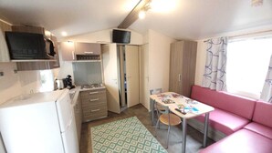 Una kitchenette compacta con microondas, estufa y armarios, una mesa de comedor con sillas y un sofá rosa junto a una ventana.