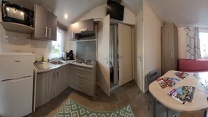Una habitación compacta con kitchenette, un comedor con mesa y asientos rosados, y un ventanal con cortinas.