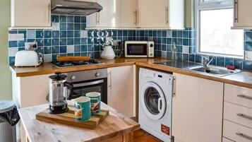Compact kitchen with microwave, toaster, and coffee maker, along with a washing machine and tiled backsplash.