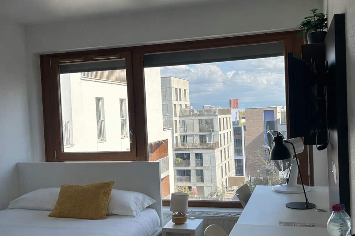 Ein modernes Hotelzimmer mit Bett, Schreibtisch, Stuhl und einem großen Fenster mit Blick auf die Stadt.