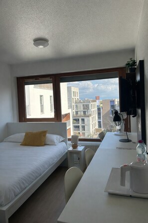 Una habitación de hotel moderna con cama, escritorio, silla y un gran ventanal con vistas a la ciudad.