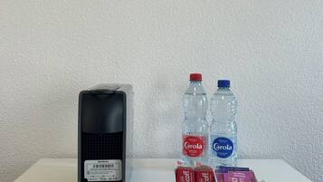 Une machine à café Krups, deux bouteilles d’eau et une boîte de capsules de café, le tout posé sur une surface blanche.