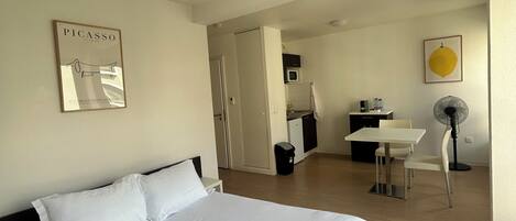 Habitación de hotel con cama, escritorio, silla, microondas y ventilador.