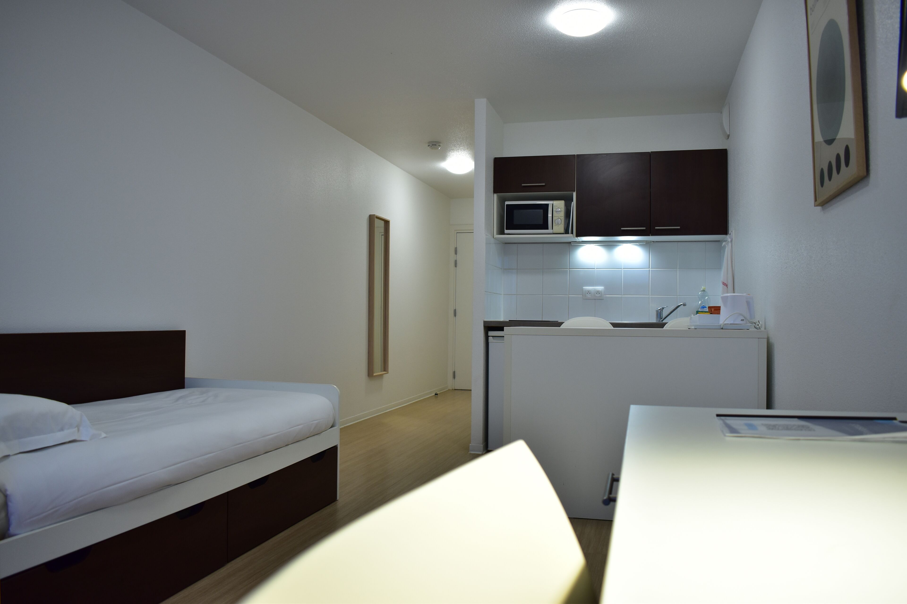 Una camera d'albergo compatta con un letto singolo, un angolo cottura e una scrivania.