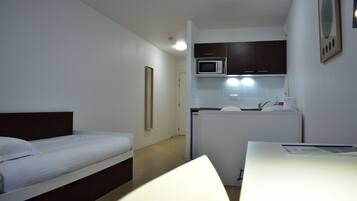 Una camera d'albergo compatta con un letto singolo, un angolo cottura e una scrivania.