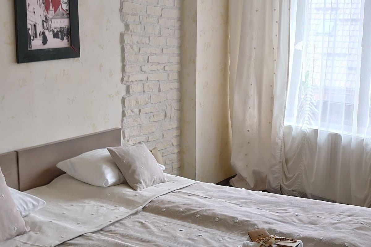 Ein Schlafzimmer mit einem Bett, einem Bild an der Wand, einer Ziegelwand und einem Fenster mit Vorhängen.