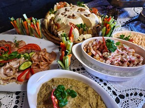 Ein Tisch mit verschiedenen Speisen, darunter ein Käselaib, Aufschnitt und eine Schüssel mit Dip.