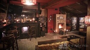 A cozy bar area with a fireplace, wooden furniture, and a red wall. - Vlahia Inn (Moieciu de Jos)