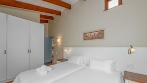 Une chambre à coucher avec un grand lit, du linge de lit blanc, une table de chevet en bois et une armoire.