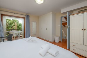 A bedroom with a bed, a small table, and a chair, a wardrobe, and a balcony with a view of greenery. - San Lameer Villa 1935 (Southbroom)