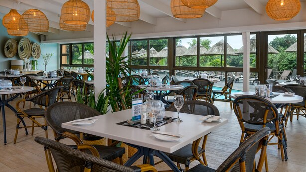 Un restaurant avec des chaises en osier, des tables blanches et des lampes en osier suspendues au plafond.