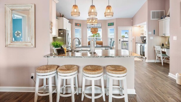 Una cocina con isla central, taburetes blancos de bar e iluminación colgante.