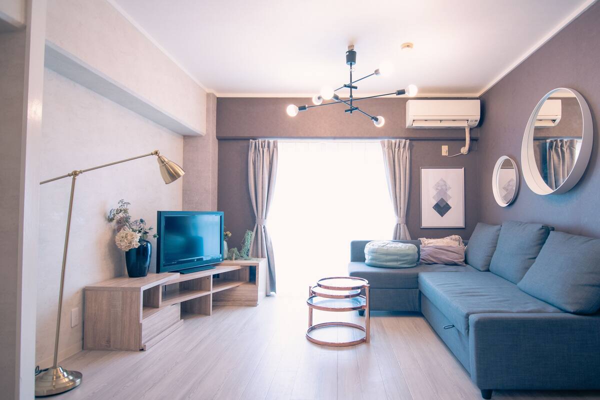 A modern living room with a flat-screen TV, a sofa, a coffee table, a floor lamp, and a large mirror.