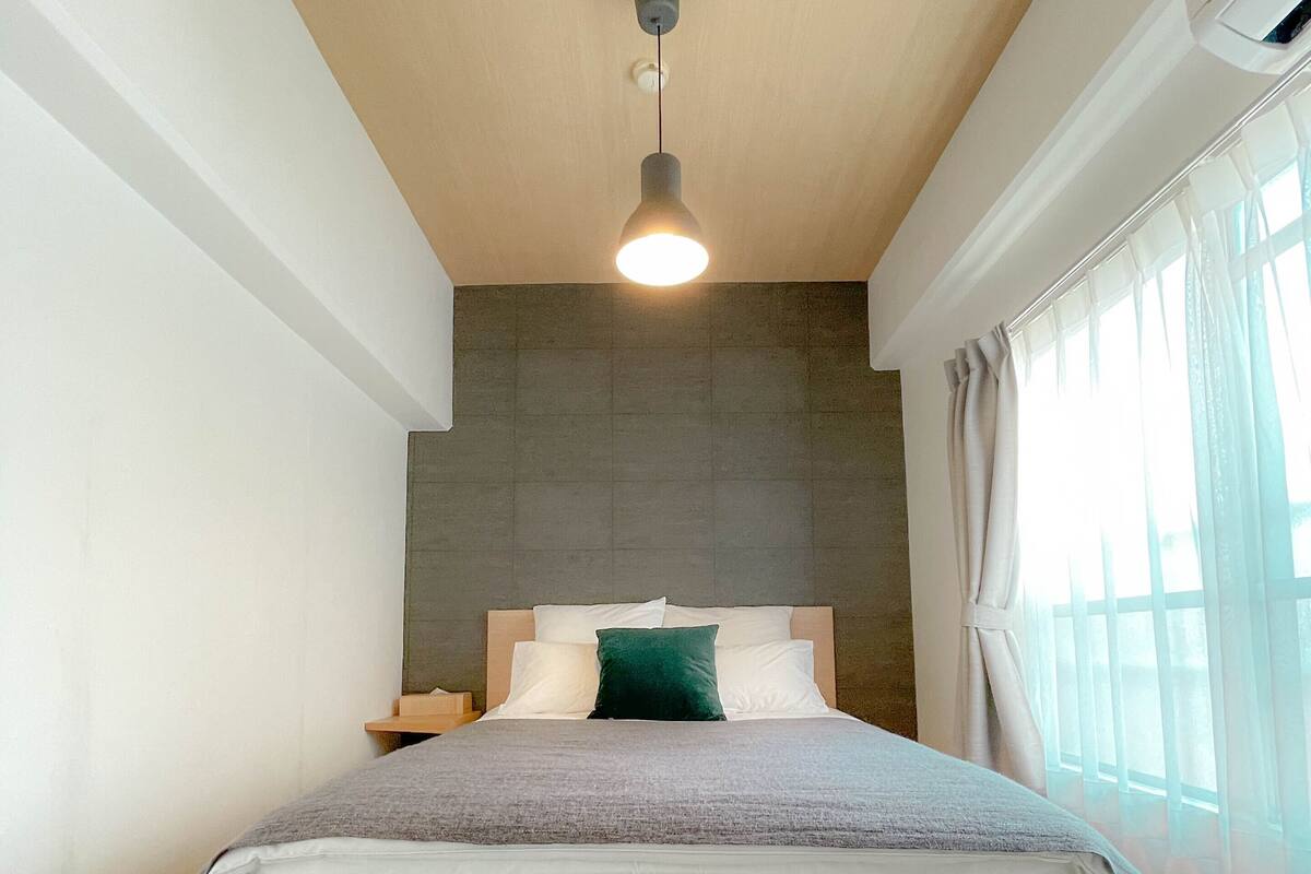 A modern bedroom with a wooden bed, a hanging light fixture, and a large window with curtains.