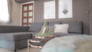 A modern living room with a grey sofa, a coffee table with a picture frame, and a decorative plant. - Staypia Condominium Namba Ebisu (Osaka)