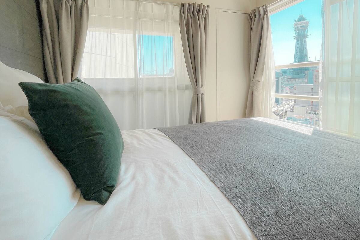 A bedroom with a large bed, a view of a cityscape through a window, and a ceiling light.