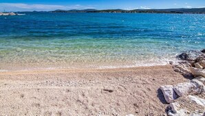 A clear beach with pebbles and rocks, calm water, and distant hills. - Sea view apartament Blue Star (Sv. Filip I Jakov)