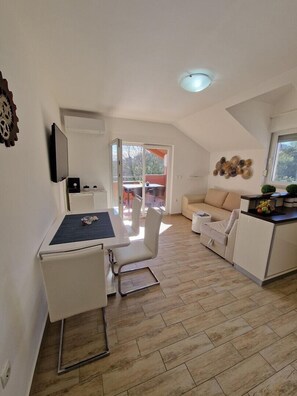 En moderne, åben stue og spiseområde med et køkken, et spisebord med stole, en sofa og en balkon med bord og stole.