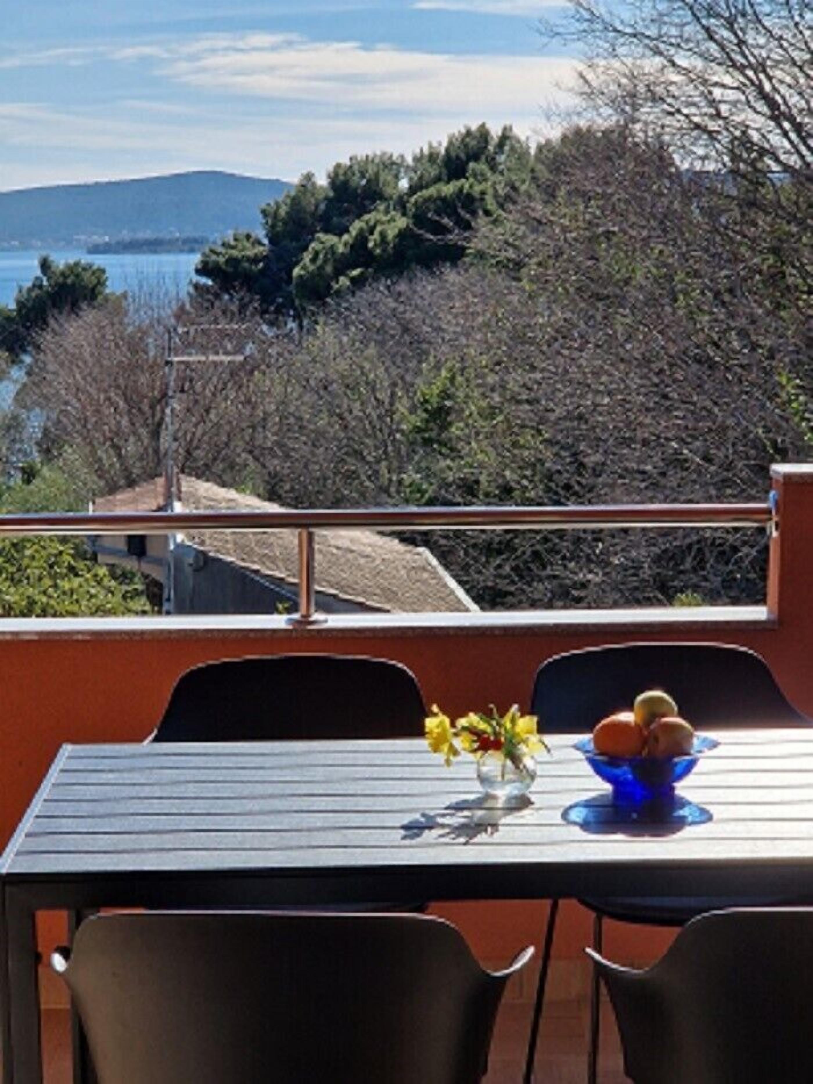 Una mesa con sillas y un frutero en un balcón con vistas al agua y colinas.