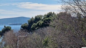 A table with chairs and a bowl of fruit on a balcony overlooking a body of water and hills. - Sea view apartament Blue Star (Sv. Filip I Jakov)