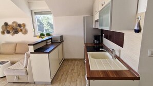A compact kitchen with a wooden countertop, a sink, and a microwave. There is a window providing natural light, and a decorative wall piece above the counter. - Sea view apartament Blue Star (Sv. Filip I Jakov)
