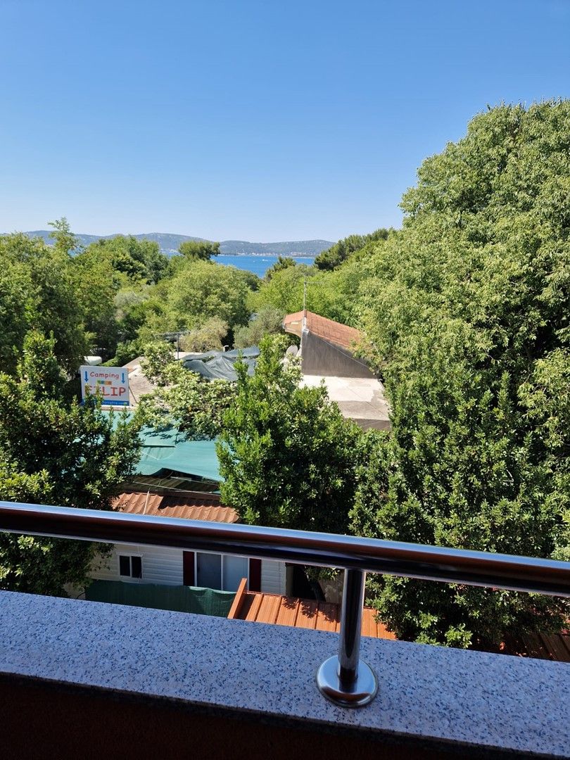 A balcony with a metal railing overlooking a residential area with houses and a clear blue sky.